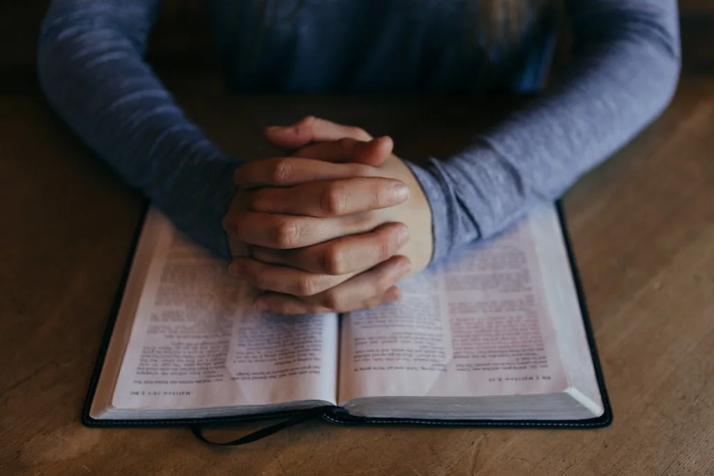 Hands folded in prayer over an open Bible